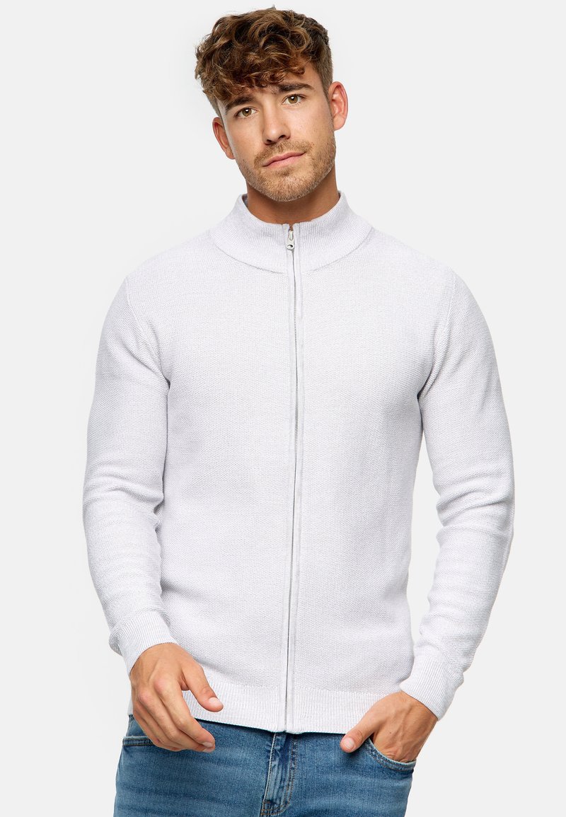 Suéter gris claro con cremallera, cuello alto, patrón de punto texturizado, diseño ajustado y puños y dobladillo acanalados. Lleva puesto sobre jeans azules.
