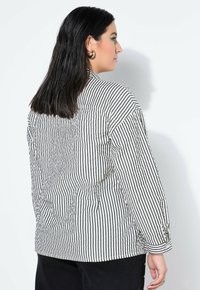 Gestreept overhemd met zwarte en witte verticale strepen, lange mouwen en een losse pasvorm, met een rugstuk en manchetten met knopen.