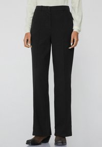 Zwarte wijde broek van gladde stof met een hoge taille, knoopsluiting en voornaaddetails. Gecombineerd met zwarte hakken.