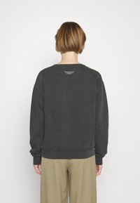 Sudadera de gran tamaño de color gris oscuro con un escote redondeado y mangas largas, con un detalle de logo texturizado en la parte posterior.