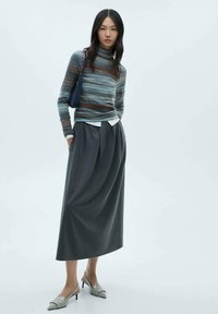 Randig polotröja i jordnära toner, kombinerad med en grå plisserad maxikjol. Silverfärgade spetsiga klackar och en liten marinblå handväska fulländar looken.