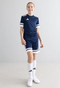 Marinblå atletisk uniform med en åtsittande tröja med vita ränder, matchande shorts, vita strumpor och fotbollsskor med svarta detaljer.