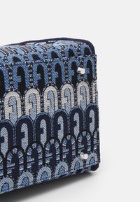 Saco de tecido texturizado com um padrão geométrico azul e preto, com acabamentos em metal prateado e uma forma retangular estruturada.