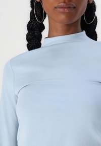 Maglia azzurro chiaro a maniche lunghe con collo alto, realizzata in tessuto morbido, con cuciture minime e una silhouette aderente.