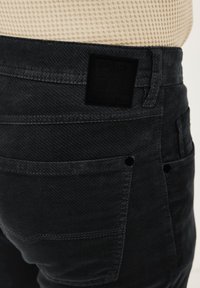 Dunkle Denim-Jeans mit strukturierter Oberfläche, fünf Taschen und einem schwarzen Lederpatch mit Logo auf der Rückseite.