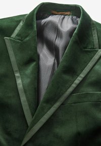Grüner Samtblazer mit Satinakzenten, einer einzelnen Tasche und Innenfutter aus Mesh. Glatte Textur, strukturierte Revers und taillierte Passform.