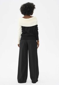 Maglione scollato in nero e crema, con una texture a coste. Abbinato a pantaloni neri a vita alta e gamba larga con righe bianche.