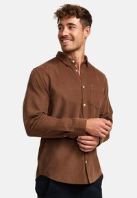 Barna, hosszú ujjú, texturált anyagból készült ing, gombos gallérral és bal oldali mellzsebbel. Klasszikus szabású, gombos díszítéssel.