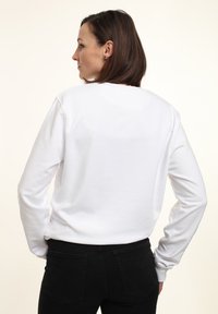 Sudadera blanca de manga larga con cuello redondo y puños acanalados. Presenta una textura suave, vista trasera y un corte recto.