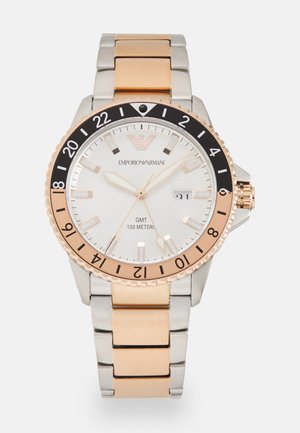 Silver and gold-tone stainless steel watch with a white dial, black bezel, and GMT function. Features a date window and luminous markers.