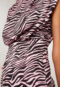 Vestido de tela con estampado de cebra en rosa y negro, con diseño drapeado y textura. Primer plano que muestra detalles del patrón y la tela.