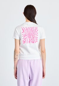 Hvit, kortermet t-skjorte med et stort rosa solstrålegrafikk og teksten "DICKIES SINCE '22" på baksiden. Glatt bomullsteksture.