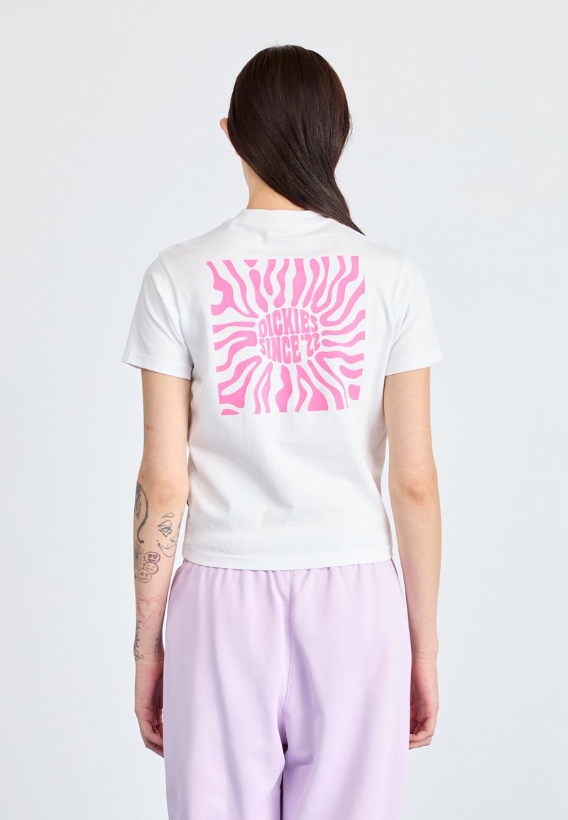 Hvit, kortermet t-skjorte med et stort rosa solstrålegrafikk og teksten "DICKIES SINCE '22" på baksiden. Glatt bomullsteksture.