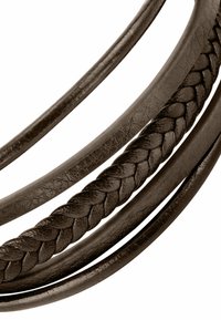 Cinture intrecciate in pelle marrone con una superficie liscia, caratterizzate da tre fasce arrotondate. La cintura centrale è distintamente intrecciata per un tocco di maggior dettaglio.