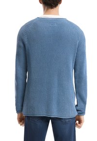 Blauer Strickpullover mit strukturiertem Muster, langen Ärmeln und Rundhalsausschnitt. Getragen mit dunkelblauen Jeans, die eine lässige Silhouette zeigen.