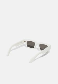 Gafas de sol rectangulares blancas con lentes cuadrados, marco de plástico suave y lentes tintados de un gris oscuro. Presentan un detalle sutil en las bisagras.