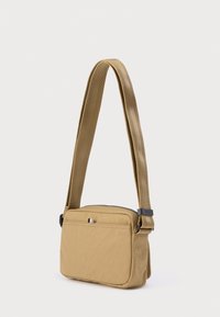 Τσάντα ώμου σε καφέ χρώμα, κατασκευασμένη από ανθεκτικό ύφασμα, ορθογώνιο σχήμα, ρυθμιζόμενο λουράκι, κλείσιμο με φερμουάρ και μπροστινή τσέπη με μικρή λεπτομέρεια λογότυπου.