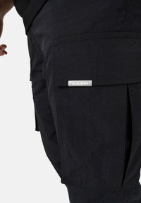 Svarte cargo-bukser med et elegant design, slitesterkt stoff, sidelommer og et sølvfarget logo-merke på forkmlommen.