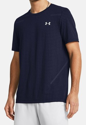 Mężczyzna ubrany w granatową koszulkę sportową z krótkim rękawem, z delikatnym wzorem w kratę i białym logo Under Armour na piersi.