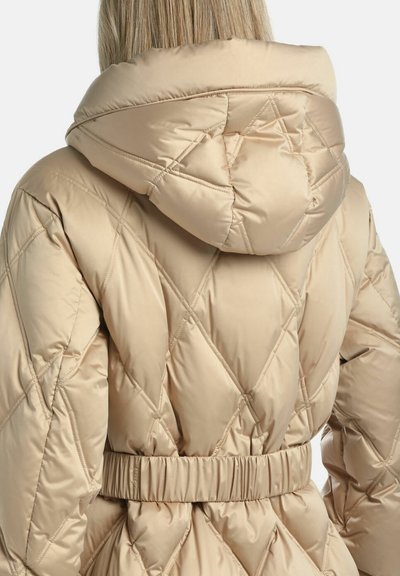 Beige quiltet pufferjakke med hætte, elastisk talje og diagonalt syning mønster. Glat stof med en blød tekstur.