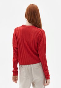 Rød ribbet sweater med lange ærmer, rund hals og en cropped design. Båret med lysebeige højtaljede bukser med baglommer.