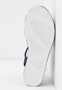 Semelle de sandale en caoutchouc blanc avec grip texturé, arborant un design incurvé et une indication de taille "37". Partie supérieure visible en textile bleu.
