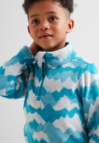 Fleece pullover with a zigzag pattern in varying shades of blue and white, featuring a stand-up collar and a half zipper. Soft texture.