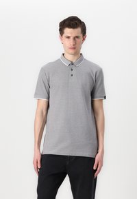 Šedé polo tričko s texturovanou tkaninou, bílým límcem a akcenty na rukávech, tříknoflíkovou légou a slim fit. Nosené s tmavými džíny.