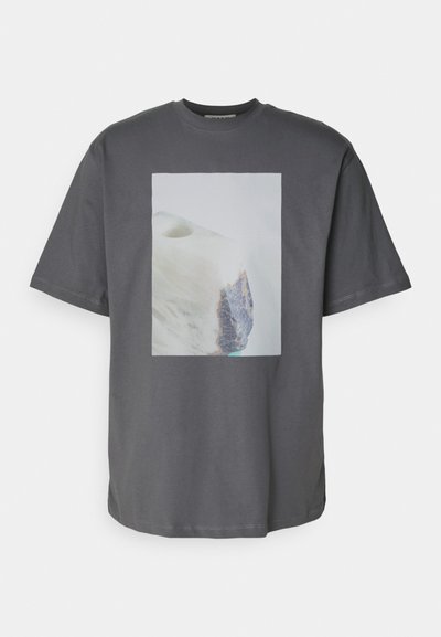 Grijze katoenen t-shirt met een rechthoekig gedrukt ontwerp, dat een gladde, lichte achtergrond en een gestructureerd, donker rokelement bevat.