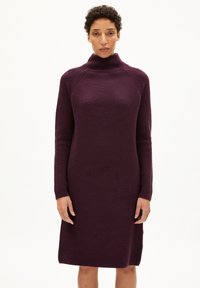 Robe en tricot de couleur violet profond avec un col montant, des manches longues et une texture côtelée ; longueur genoux avec un détail de fente sur le côté.