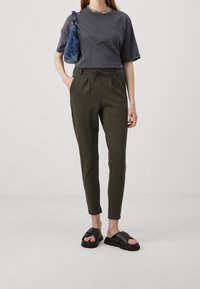 Mörkgrå kortärmad t-shirt, olivgröna tapered byxor med dragsko och svarta sandaler med korsremmar; blå mönstrad väska.