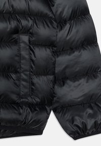 Czarna kurtka puchowa z pikowanymi sekcjami, gładką nylonową tkaniną, wewnętrzną kieszenią oraz ściągaczami na mankietach. Miękka w dotyku z lekką izolacją.