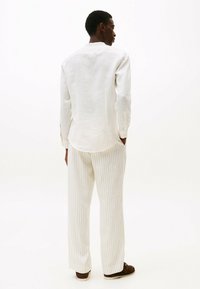 Camisa blanca de lino de manga larga con un cuello redondo, combinada con pantalones de pierna ancha a rayas beige. Calzado casual completa el atuendo.