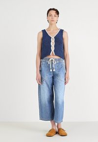 Blå strikket crop topp med hvit kant og knappedetalj, kombinert med lyseblå vide jeans og brune slip-on sko.