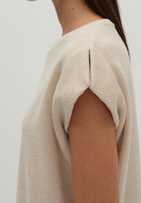 Beige texturerad stickad topp med korta ärmar, med en subtil sidosprick och ribbade detaljer, designad för en avslappnad passform.