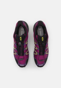 Tênis de atletismo roxos e pretos com um cabedal de malha texturizada, detalhes em amarelo contrastante, sistema de atilhos integrado e sola acolchoada.