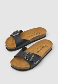 Svarta lädersandaler med två breda remmar, varav en har en silverspänne. Korkinsats med ljusbrun textur och tryckt logotyp.