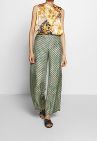 Blomstermønsteret ærmeløs top med høj hals kombineret med vide grønne mønstrede bukser og sorte slide-sandaler.