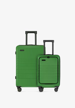 Twee groene harde koffers van verschillende maten met verticale groeven, zwarte accenten en uitschuifbare handvatten; op wielen voor mobiliteit.