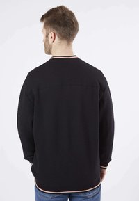 Sweatshirt noir avec un motif texturé et matelassé. Doté d'un col et de poignets à rayures contrastées. Coupe ample avec un ourlet et des manches côtelés.