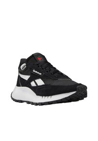 Baskets Reebok noir et blanc avec dessus en suède et mesh, semelle blanche épaisse et logo rouge sur la languette, légèrement inclinées vers la droite.