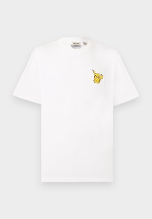 T-shirt blanc à manches courtes avec un petit motif jaune de Pikachu sur le côté gauche de la poitrine et une étiquette Pokémon à l'intérieur du col.