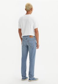 Blå denim jeans med rett snitt, middels vask og en lærpatch bak. Satt sammen med en enkel hvit t-skjorte og blå sneakers.