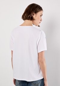 Hvid kortærmet t-shirt, rund halsudskæring, afslappet pasform, glat bomuldsstof, med en lille logo detalje på ærmet.