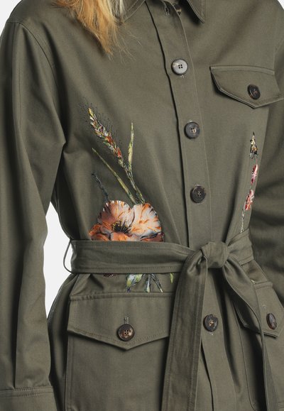 Olive green button-up jacket with a waist tie, front pockets, and floral embroidery on the chest and sides.