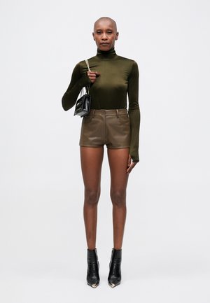 Pulover verde măsliniu cu guler înalt, pantaloni scurți din piele maro, cizme negre până la gleznă cu accente aurii ascuțite și o geantă mică din piele texturată neagră.