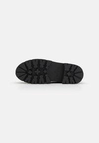 Semelle de chaussure en caoutchouc noir avec une texture rugueuse et un motif de semelle prononcé, portant le nom de la marque "GUESS" et la taille "37."