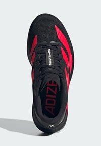 Scarpe sportive nere con accenti rossi, sopra in tessuto, design testurizzato, dotate di un colletto imbottito e suola in gomma. Logo "ADIZERO" sulla linguetta.