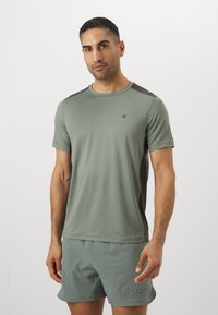 T-shirt atlético verde-claro de mangas curtas com detalhes escuros nos ombros. Apresenta um pequeno logótipo no peito. Combinado com calções a condizer.