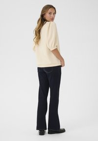 Krämfärgad tröja med puffärmar, i kombination med mörka utsvängda jeans. Outfiten har en avslappnad passform och minimalistisk design. Svarta skor fulländar looken.